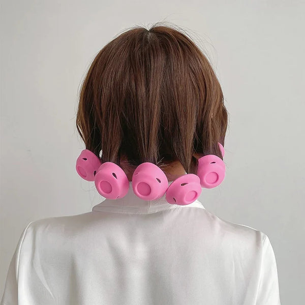 Brown hair styled with pink pig-shaped hair rollers, shown from the back on a model wearing a white shirt against a light gray background.